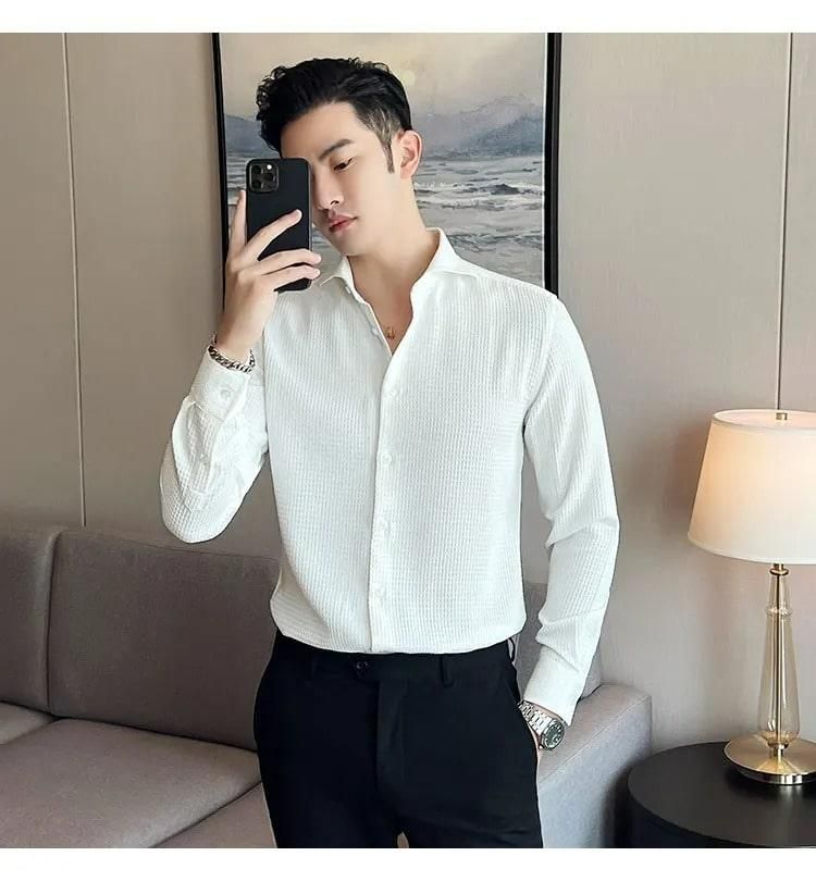 Man taking a mirror selfie wearing a white shirt and black pants in a room with a lamp and sofa.